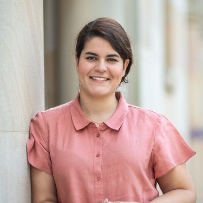 A woman leaning against a wall wearing a pale pink shirt 